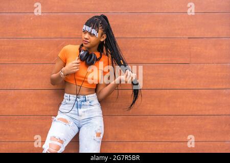 Native American trap dancer with braids in an orange shirt and jeans standing by the wall Stock Photo