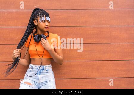 Native American trap dancer with braids in an orange shirt and jeans standing by the wall Stock Photo