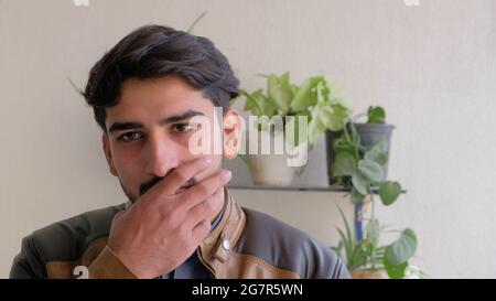 Handsome Indian man looking at something  against a wall with plants in pots Stock Photo