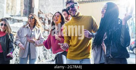 Group of young Friends gathering in the street listening music from smartphone and dancing together. Multiracial millennials having fun outdoors jokin Stock Photo