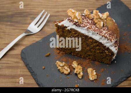Closeup of a single serving of a carrot cake with walnut chunks on a slate plate next to a small fork Stock Photo