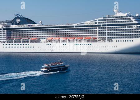 Santorini island - Greece - October 3 2018 : Large cruising ship moored at sea. Small boat sailing in foreground. Stock Photo