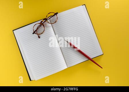 Lined notebook with Vintage red pen with nib and old glasses, isolated on yellow background, copy space Stock Photo