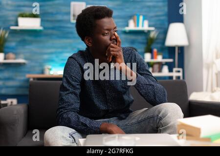 Portrait of stressed, pensive african american man looking out the window thinking about business problems. Adult man in living room working from home office desk. Serious black person Stock Photo