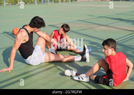 Three brothers doing leg stretching exercises, one of them has a leg prosthesis. Siblings stretching before playing basketball. Stock Photo