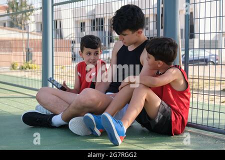 Three brothers looking something on the smartphone sitting on floor wearing sport clothes. Stock Photo