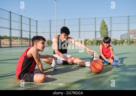 Three brothers doing leg stretching exercises, one of them has a leg prosthesis. Siblings stretching before playing basketball. Stock Photo