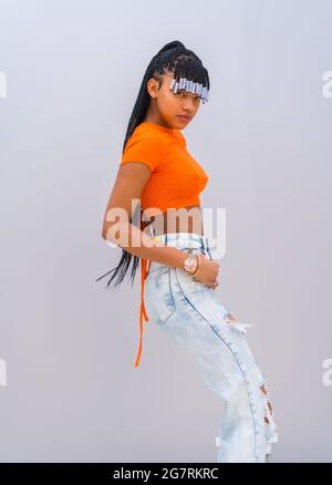 Native American trap dancer with braids wearing an orange shirt and jeans posing by the white wall Stock Photo