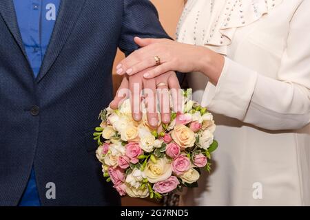 Bride and groom holding hands showing their rings, wedding couple holding bouquet Stock Photo