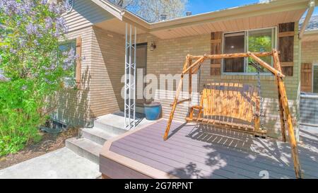 Pano Home facade with wooden swing bench on the porch deck on a sunny neighborhood Stock Photo