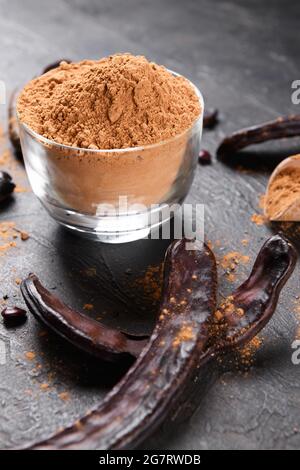 Dry carob pods and carob powder on a dark background. Organic healthy ingredient for vegan vegetarian food and drinks, close up Stock Photo