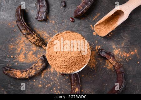Dry carob pods and carob powder over dark background. Organic healthy ingredient for vegan vegetarian food and drinks, view from above Stock Photo