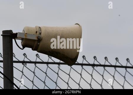 A weathered megaphone, public address speaker next to a security fence Stock Photo