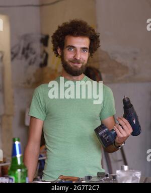 Young smiling bearded repairman standing at the worktable with a drill in a hand at his bike repair shop. July 23, 2019. Kiev, Ukraine Stock Photo