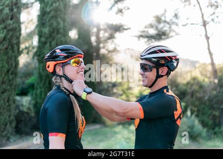 Man fastening the bicycle helmet of a young cyclist in nature at sunset. Stock Photo