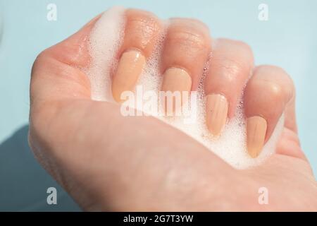 female hand with white soapy foam on a light blue background. Stock Photo