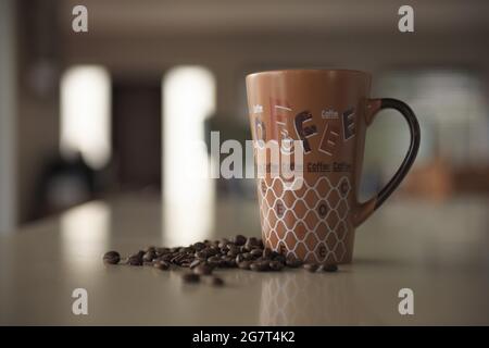 A brown cup and some scattered coffee beans sit on a kitchen counter Stock Photo