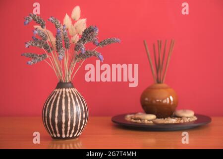 A vase of lavender and aroma diffusion sticks on a wooden table with a red background Stock Photo