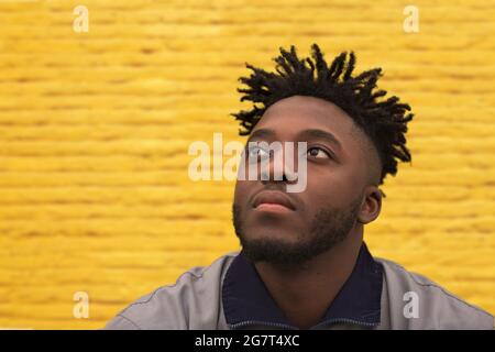 A young, confidant African man looks ahead while sitting in front of a yellow wall Stock Photo