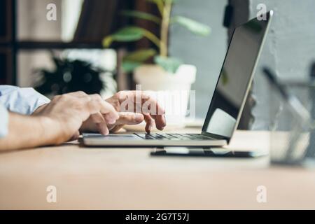 Cropped image of male hands on keyboard of laptop typing text or message. Side view. Stock Photo