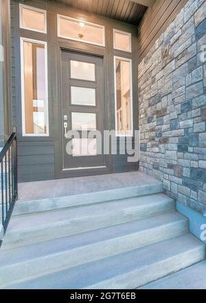 Vertical Home facade with stone brick wall and gray front door with frosted glass panels Stock Photo