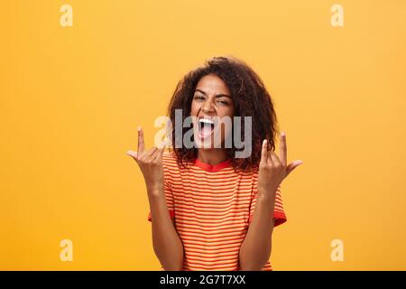 Waist-up shot of amazed happy stylish african american woman feeling awesome rocking on party yelling from joy and satisfaction showing rock n roll Stock Photo