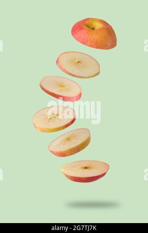 Sliced red apple flying on light green background. Levitation of fruit floating in the air. Creative minimal concept . Stock Photo