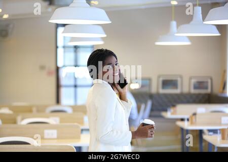 business black skin woman talking on mobile phone and holding coffee cup in office. Stock Photo