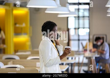 business black skin woman talking on mobile phone and holding coffee cup in office. Stock Photo
