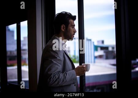 businessman drinking coffee while standing by window. Stock Photo