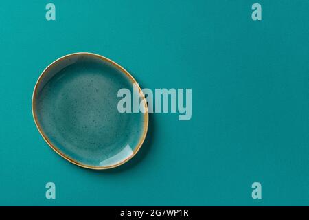 Oval turquoise blue ceramic plate with brown border over textured teal background. Modern dishes of teal trendy color for stylish food design. Stock Photo