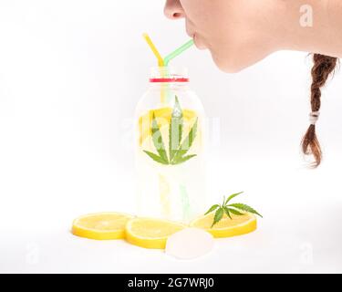 Girl drinking a cooling lemon cocktail with marijuana from a straw on white background. Stock Photo