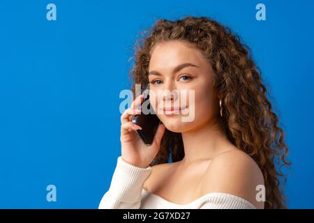 Young curly woman talking on the phone against blue background Stock Photo