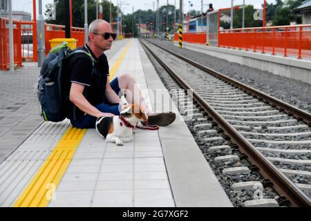 Man and his dog waiting for train on railway station platform. Older backpacker waiting for train. Journey, travel, vacation, lifestyle concept Stock Photo