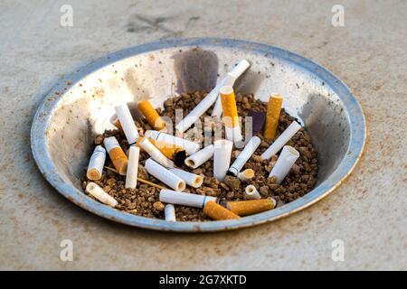 Close up of cigarettes butts in metal ashtray on street. Concept of many cigarette debris after smoking. Stock Photo