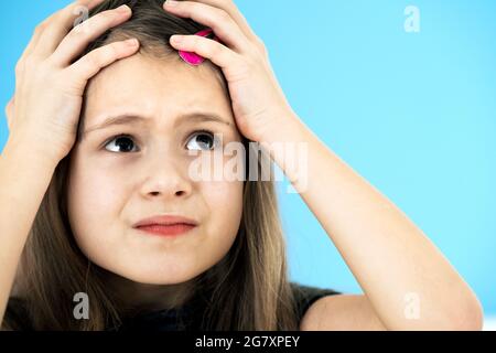 Close up portrait of upset and pensive little girl with cute pink hairpin on blue background. Stock Photo