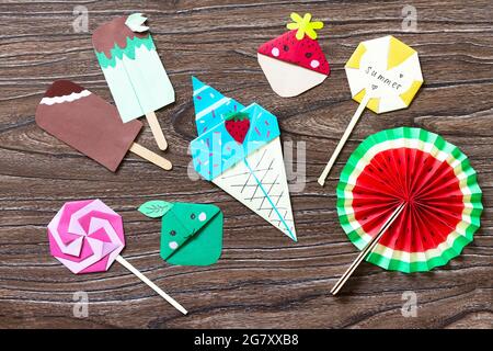 Funny toy lollipop, watermelon, ice cream and bookmarks strawberry and apple. Summer paper toy wooden sticks on a wooden table. Childrens art project, Stock Photo