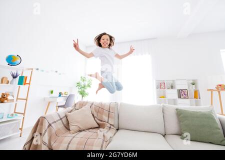 Full size profile side photo of young little girl happy positive smile jump show peace cool v-sign tongue-out grimace home Stock Photo