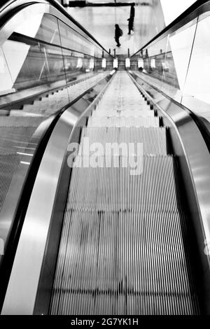 Escalator in office building with three people, strong perspective lines, looking down. Stock Photo