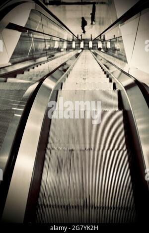 Escalator in office building with three people, strong perspective lines, looking down. Stock Photo