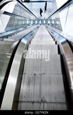 Escalator in office building with three people, strong perspective lines, looking down. Stock Photo