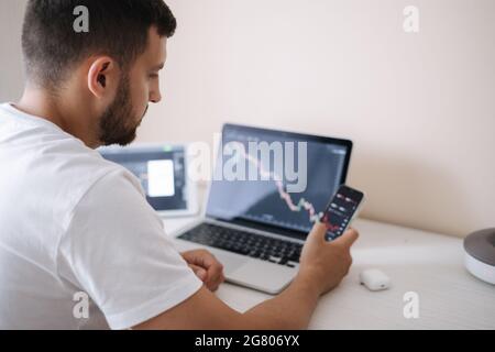 Young adult man trading on line with tablet pc connected to stock market. People, finance, investments. Over the shoulders Stock Photo