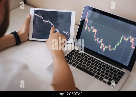 Young adult man trading on line with tablet pc connected to stock market. People, finance, investments. Over the shoulders Stock Photo
