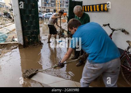 Bad Neuenahr, Germany. 16th July, 2021. Three men push mud from a cellar into a backyard with washed up vehicles. Massive rainfall has caused flooding in Bad Neuenahr in Rhineland-Palatinate as well as in the whole district of Ahrweiler. Credit: Philipp von Ditfurth/dpa/Alamy Live News Stock Photo
