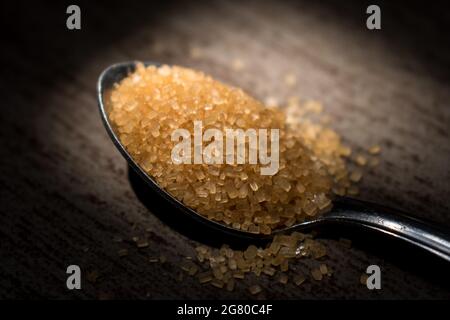 Close up of some little sugar granules on a silver spoon on a wooden table Stock Photo