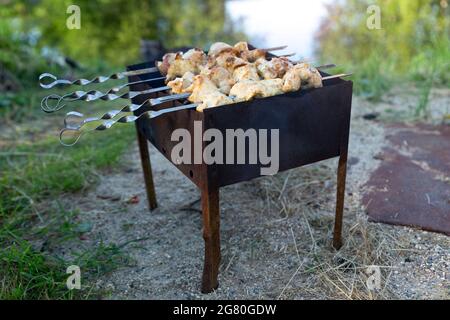 Skewered meat is fried on charcoal close-up on a grill or brazier. Picnic, evening with friends and family, cooking over an open fire in the front or Stock Photo