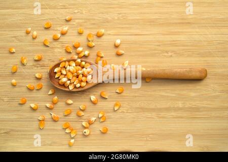 Yellow maize corn kernels ready for making popcorn, on cutting board bamboo and in wooden spoon Stock Photo