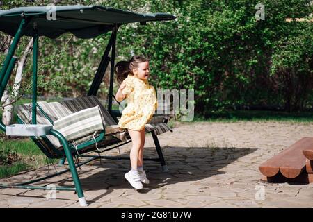 a happy laughing girl jumps from a garden swing, a girl has a good time in the backyard and on a swing in the summer Stock Photo