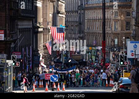 Glasgow, Scotland, UK. 16th July, 2021. PICTURED: Huge crowds of people and onlookers watch the filming. Day 4 of filming of Hollywood blockbuster movie of Indiana Jones 5. Todays scenes say a ticker tape parade with marching bands, waving crowds, press and the returning astronauts in a 1959 American New York scene. The streets are decorated with stars and strips flags and bunting and the Harrison Ford double was seen riding horse back through the streets of Glasgow. Credit: Colin Fisher/Alamy Live News Stock Photo