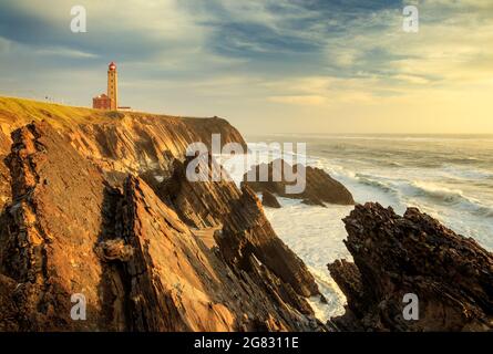 Beautiful landscape of the Penedo da Saudade Lighthouse in São Pedro de Moel, Portugal, at sunset with the cliffs and ocean waves in the foreground. Stock Photo